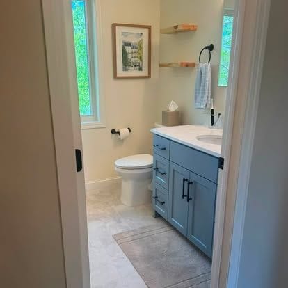 Bathroom with a navy shaker vanity, white quartz top, floating wood shelves, and a window