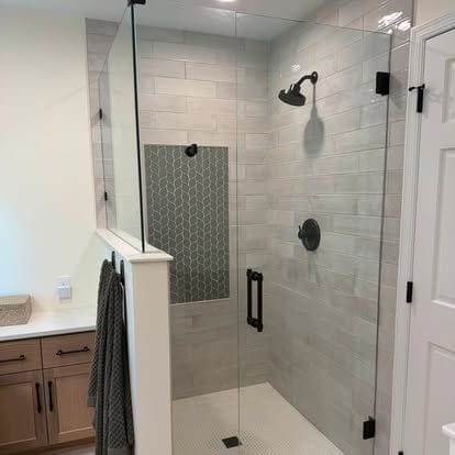 Walk-in tiled shower with a glass panel, black fixtures, and a wood vanity with white top