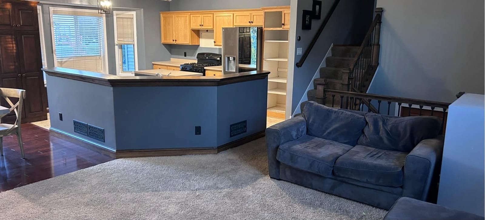Kitchen before remodel: raised bar with blue-painted base, oak cabinets, black range, carpeted living area and a stairway