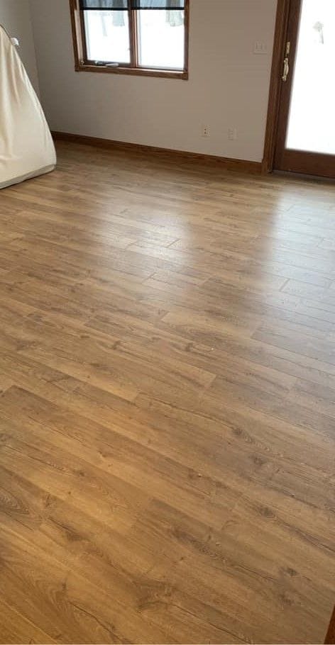 Room with new wood-look laminate plank flooring, oak base trim, and an oak entry door