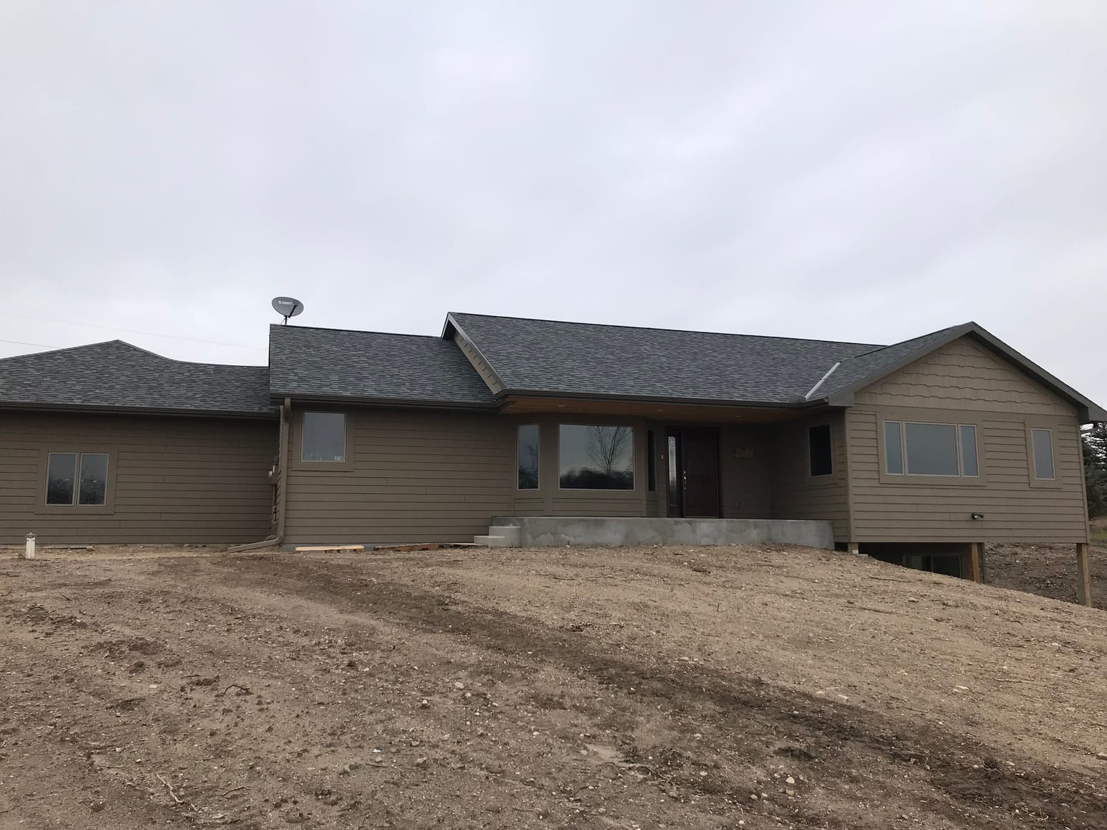 Newly built single-level house with gray lap siding and a dark shingled roof on freshly graded ground
